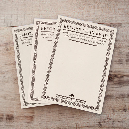 Three vintage-style notepads fanned out on a light wood background. The notepads are off-white with ornate dark borders and the title 'BEFORE I CAN READ' printed at the top.