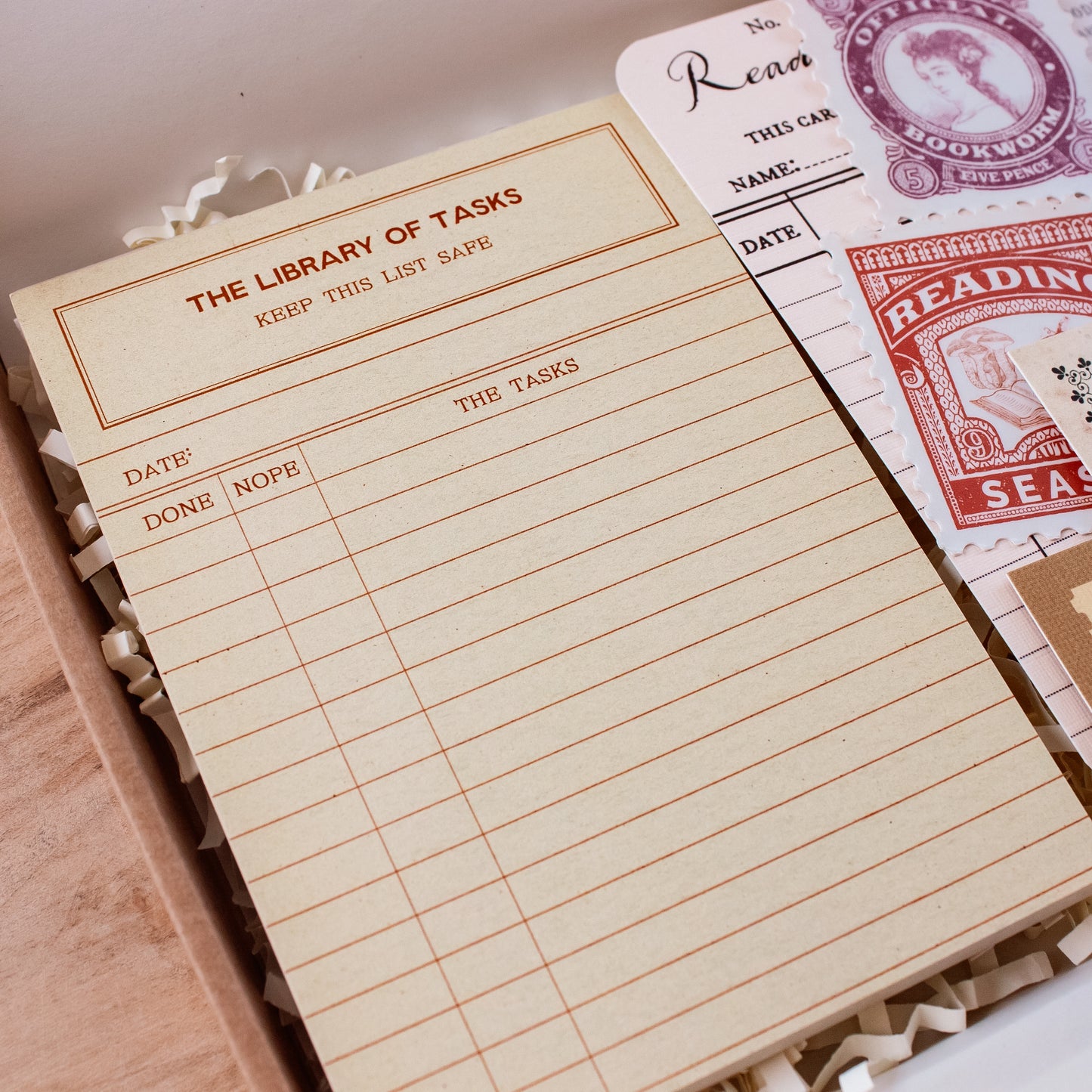 A yellow notepad with a vintage library task list design, displayed in a box with shredded paper and other retro-themed stationery.