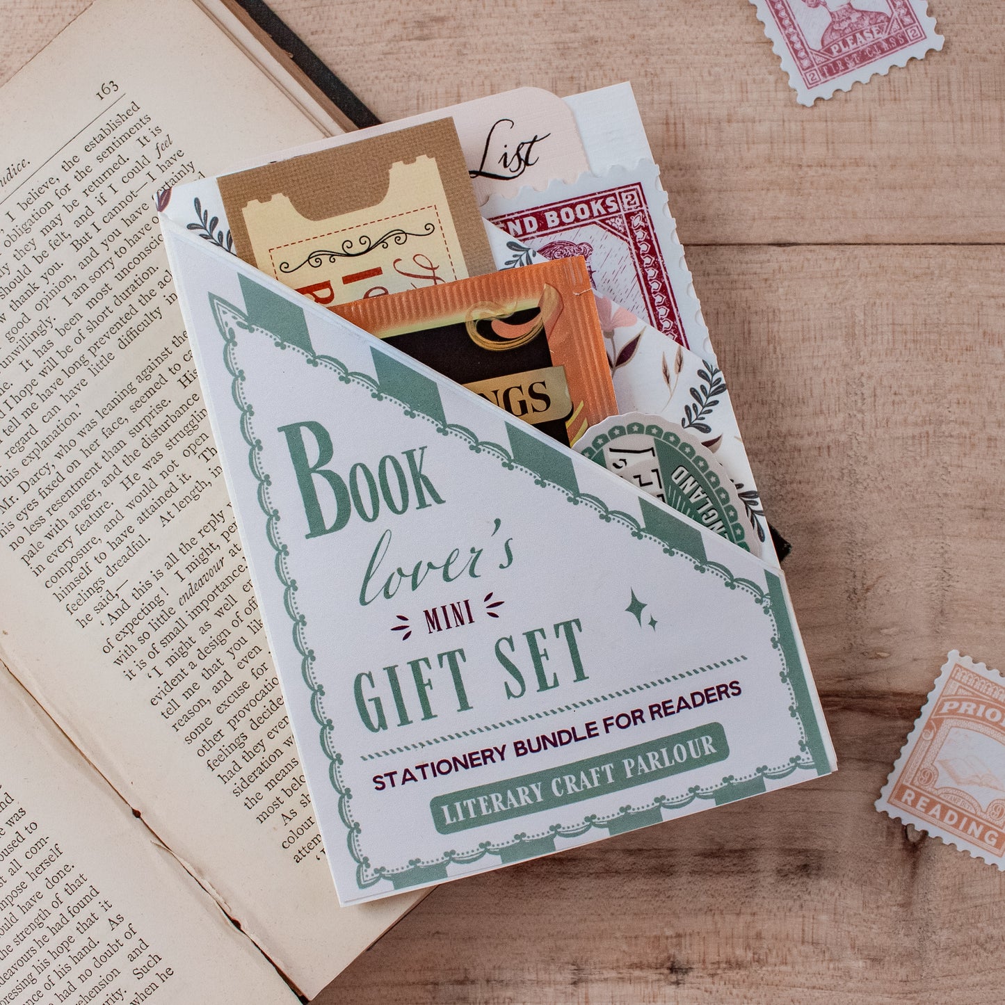 A book lover's mini gift set stationery bundle for readers, styled on a wooden tabletop next to an open vintage book with decorative postage stamps.