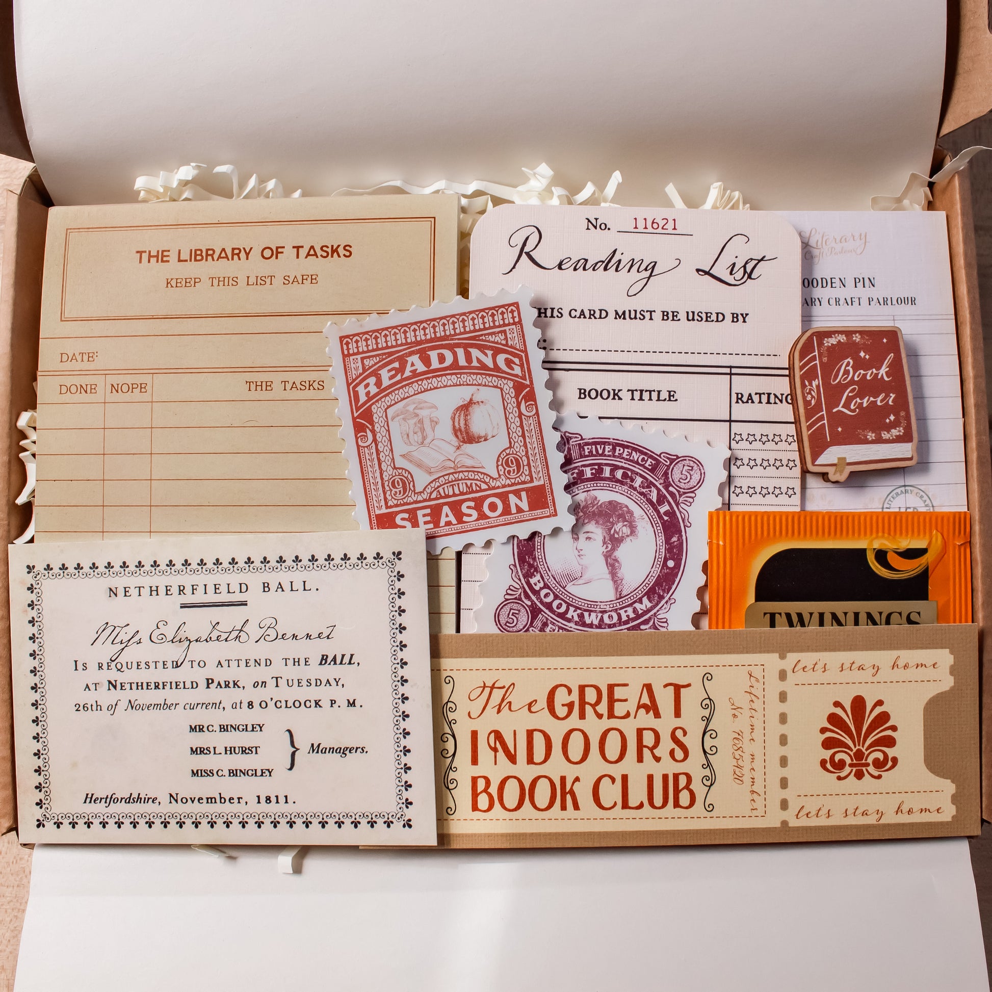 A curated bookish stationery set arranged inside a gift box, including a reading list bookmark, library card notepad, wooden book lover pin, vintage-style reading list, book club ticket bookmark, and other themed paper items.