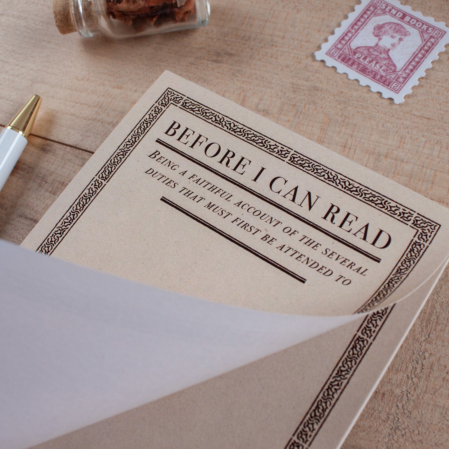 A vintage-style notepad with a cream cover and black decorative border, shown open on a wooden tabletop. The cover reads, 'BEFORE I CAN READ' with smaller text below reading "being a faithful account of the several duties that must first be attended to" leaving blank space underneath for the user to write their own lists and thoughts.