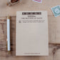 A styled flat-lay of a notepad titled 'Chapter 1. THE MATTERS AT HAND' on a wooden tabletop. The notepad is designed to look like the first page of a vintage book and starts with the quote "It was an unfortunate truth that there were things to be done before I could read..." then leaving blank space for the user to write their own to-do list making it seem like their to-do list is the start of an epic tale. It is styled on a wooden desk with a white and gold pen and  vintage postage stamps.