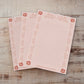 Three pink lined notepads with a rose gold floral border and corner accents, arranged on a rustic wooden surface.